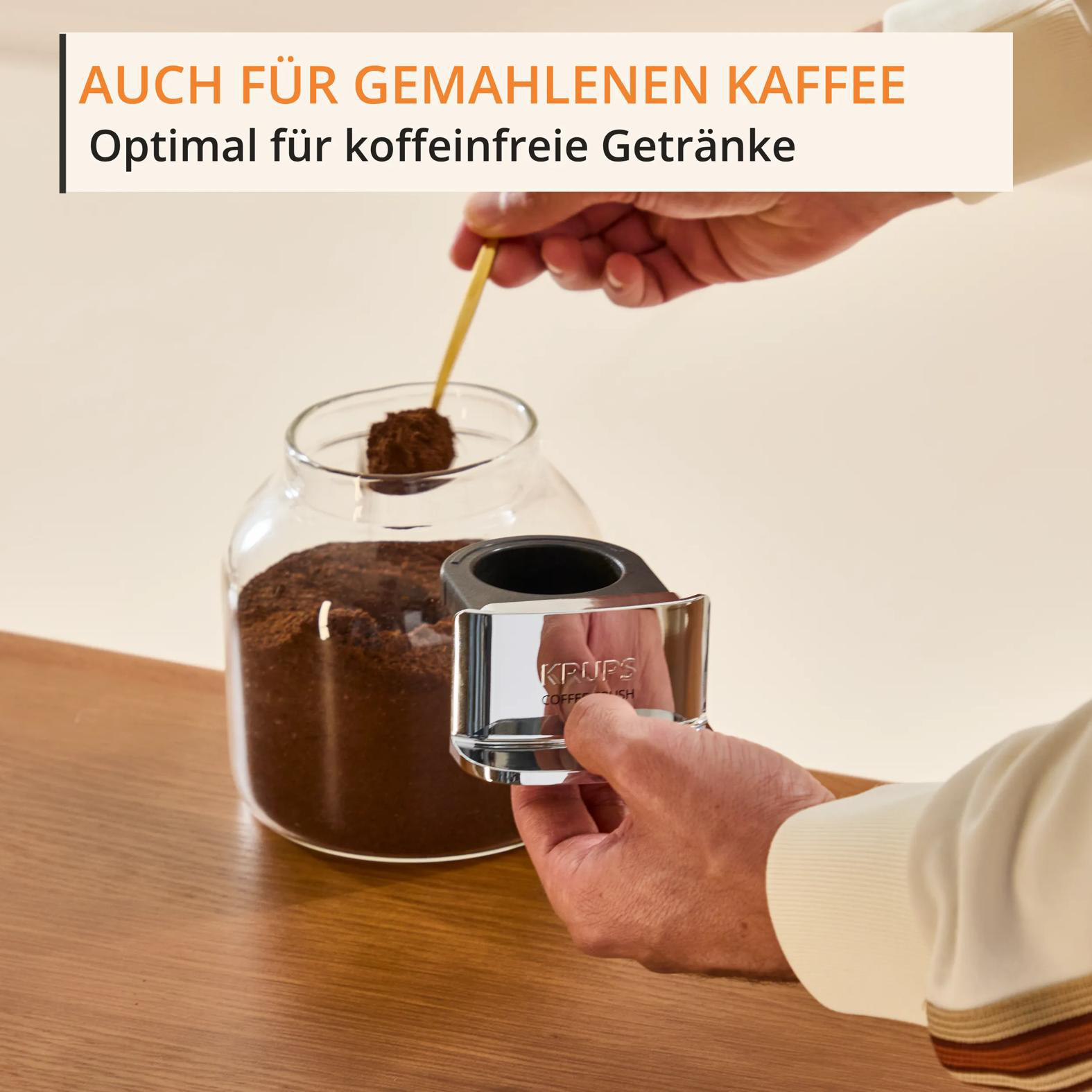Eine Hand schöpft Kaffeepulver mit einem Löffel aus einem Glasbehälter.