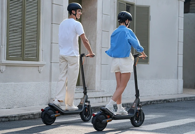 Dwie osoby w kaskach jadą hulajnogami elektrycznymi ulicą.