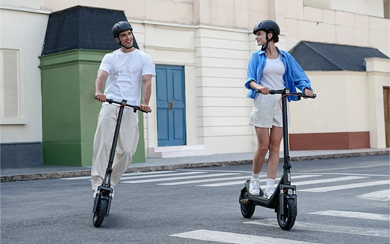 Mężczyzna i kobieta jadą na hulajnogach elektrycznych po ulicy.