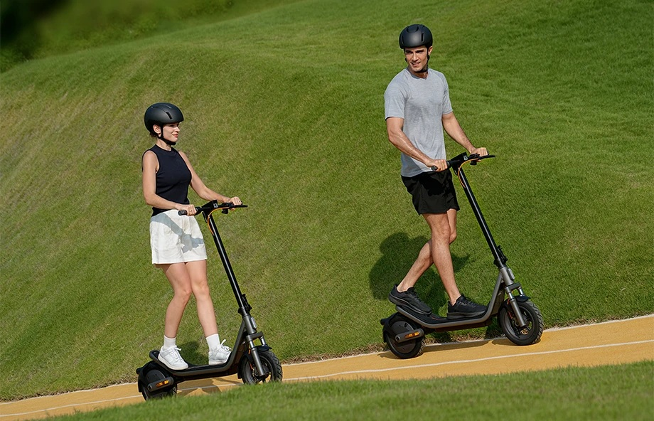 Dwie osoby jadą na hulajnogach elektrycznych po żółtym torze przez zieloną trawę.