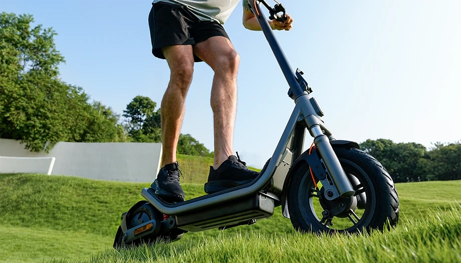 Mężczyzna jedzie na hulajnodze elektrycznej po zielonym wzgórzu na zewnątrz.