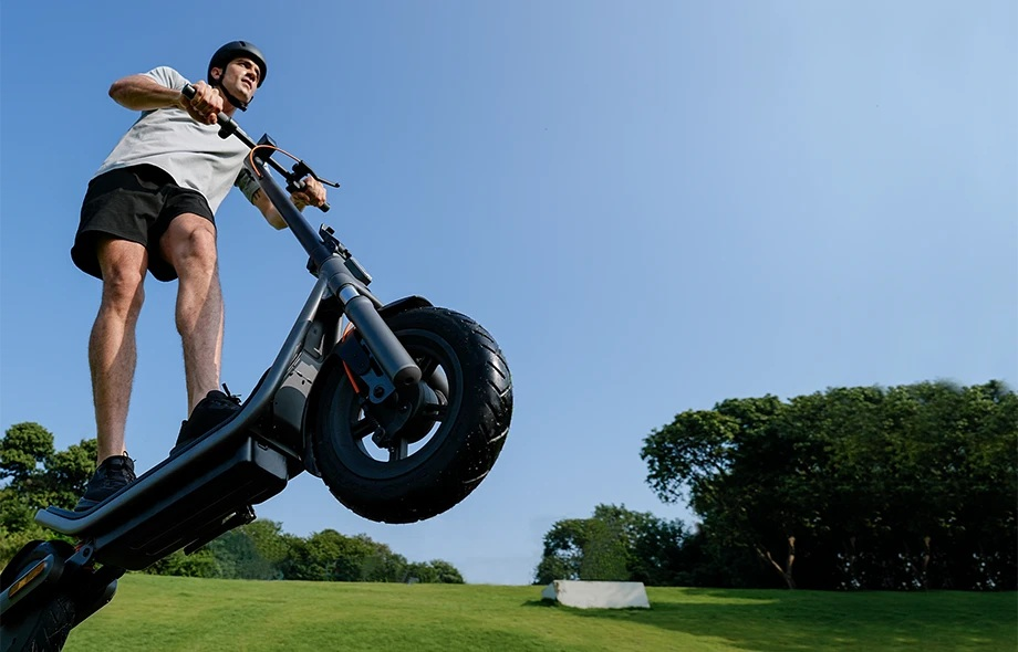 Mężczyzna na hulajnodze elektrycznej jedzie przez park.