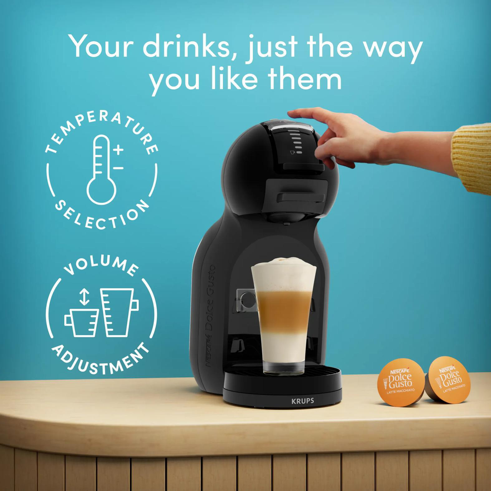 Eine schwarze Kaffeemaschine mit einem Glas Latte Macchiato und Kapseln.