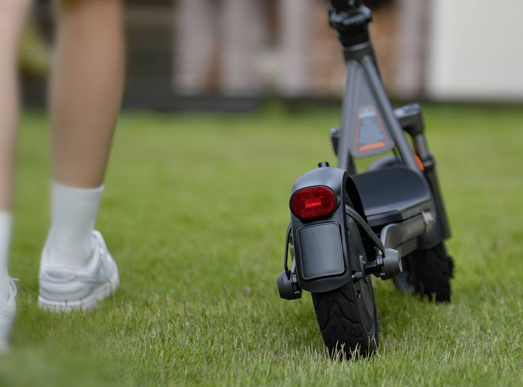 Zbliżenie na hulajnogę elektryczną na trawie, z nogami w białych butach.