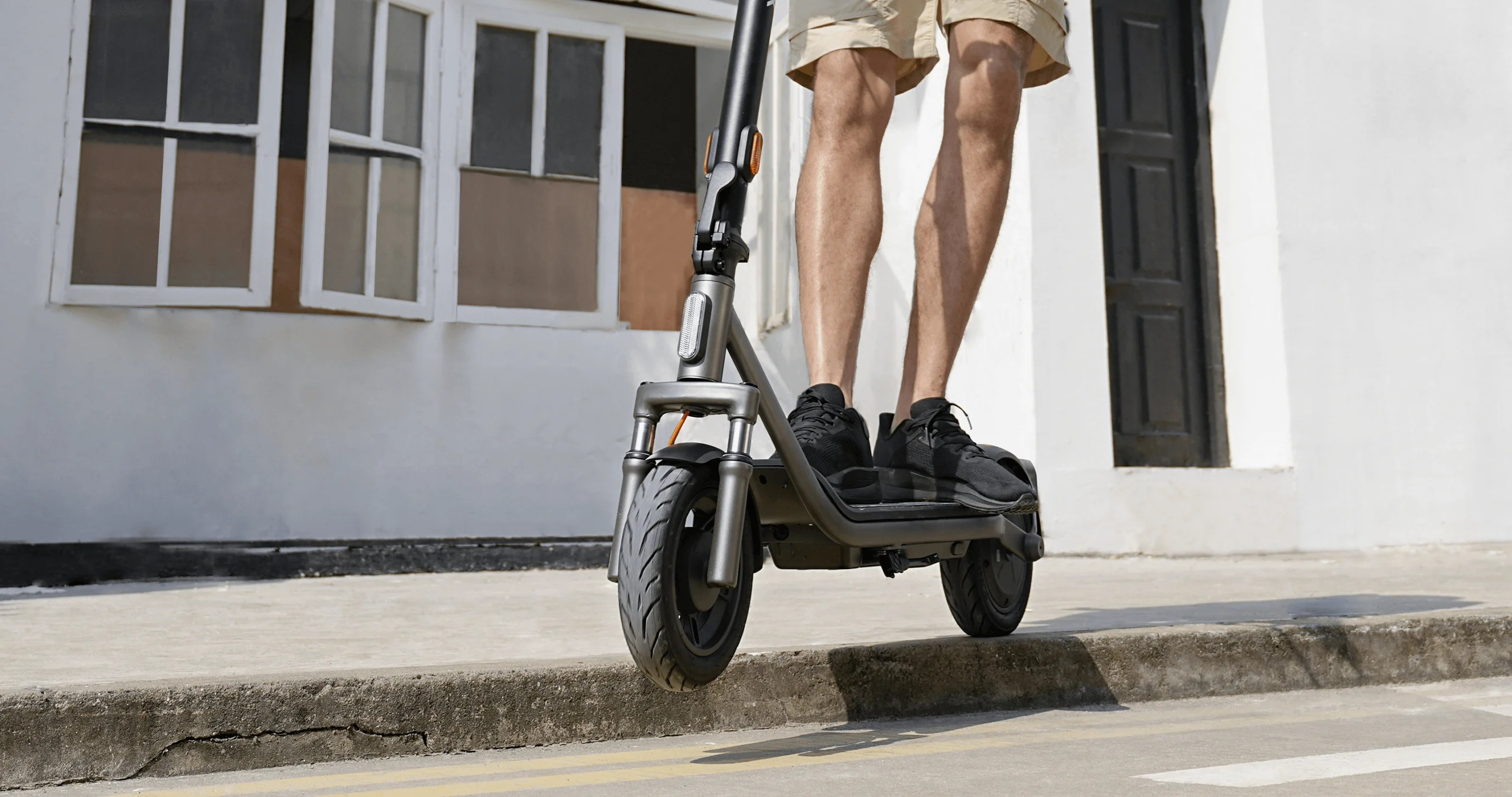 Mężczyzna jedzie na hulajnodze elektrycznej po chodniku z budynkiem w tle.