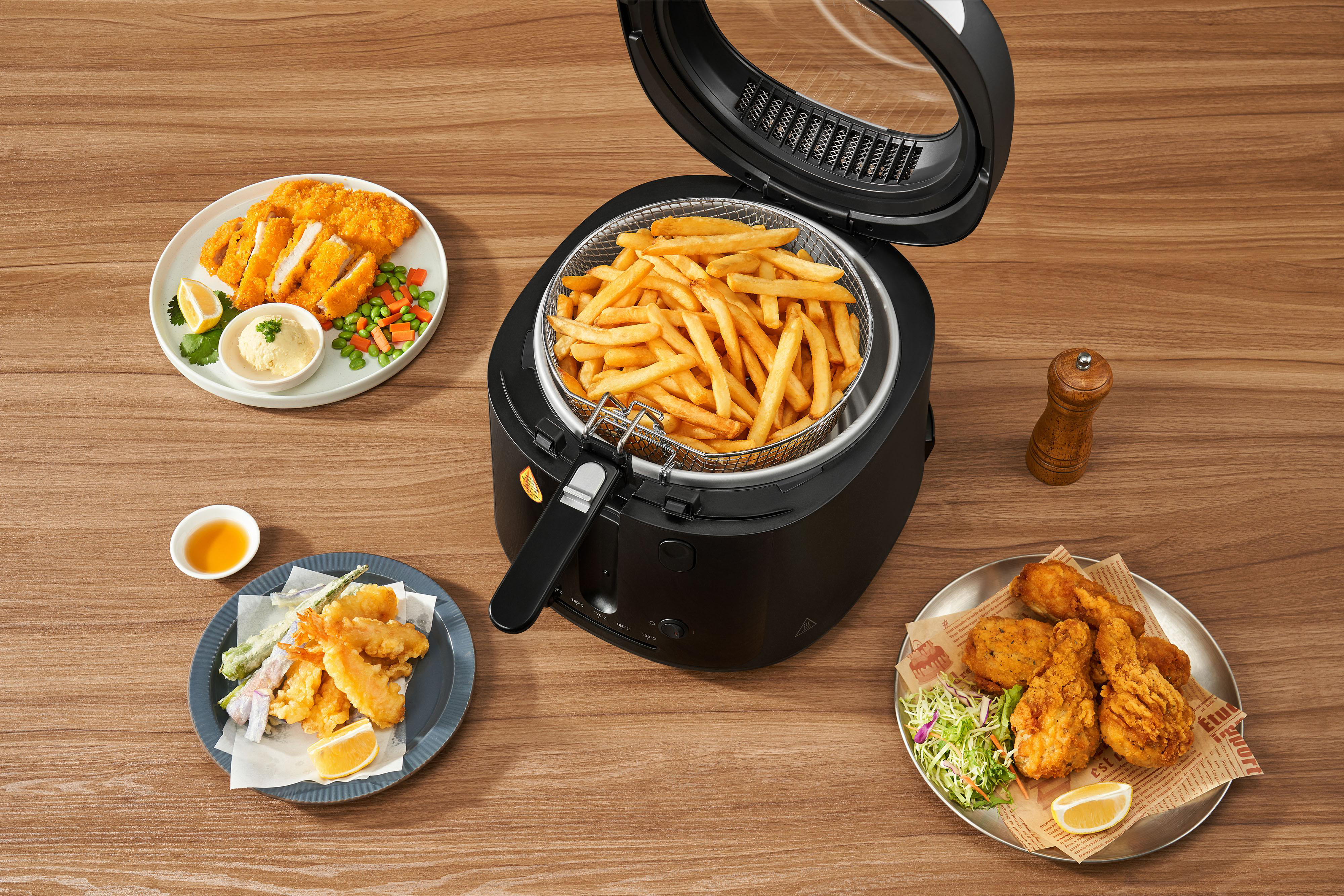 Eine Heißluftfritteuse mit Pommes daneben, Hähnchen und Tempura auf Tellern.