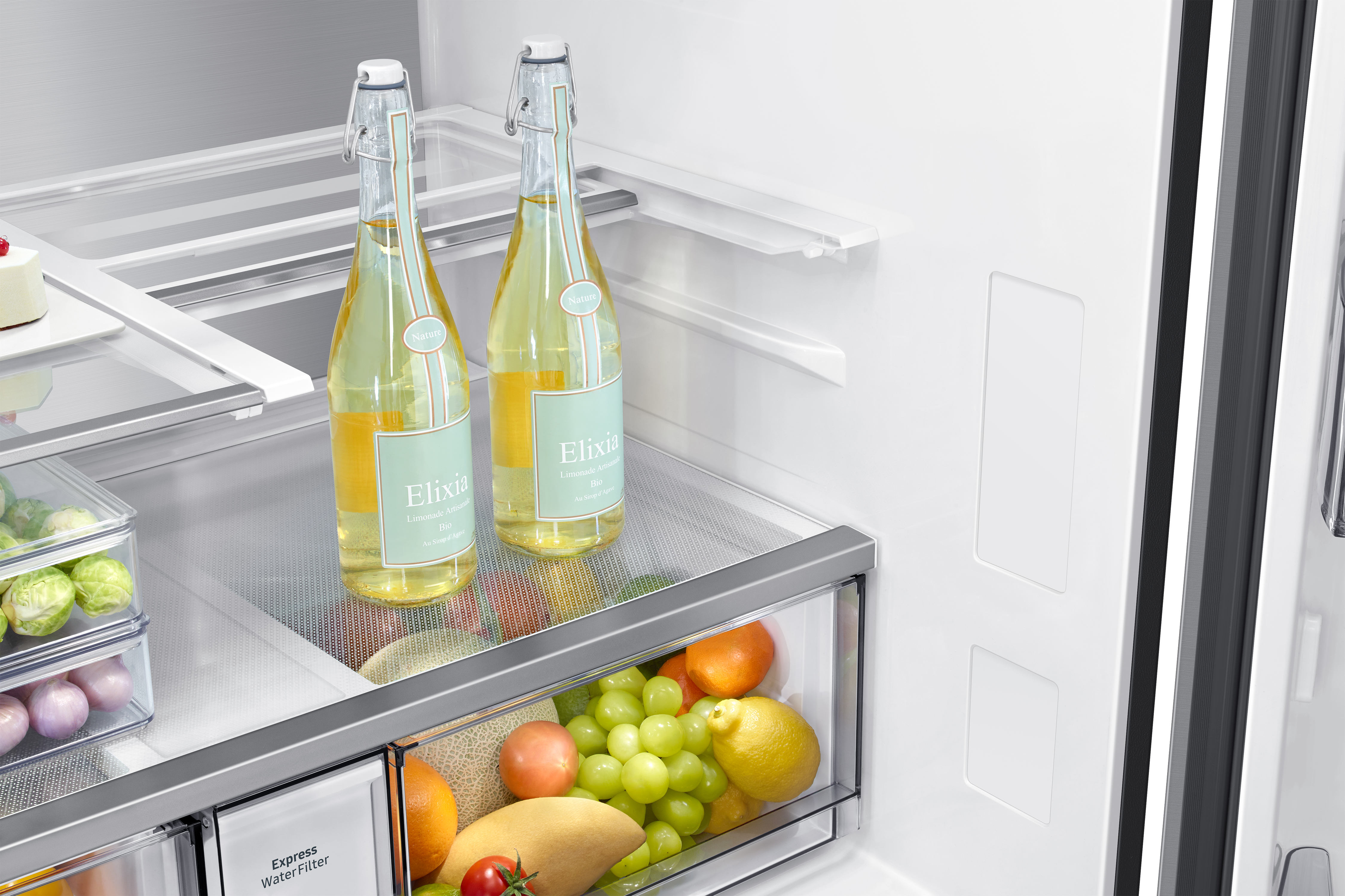 Dos botellas de limonada Elixia en un estante de refrigerador sobre frutas y verduras.