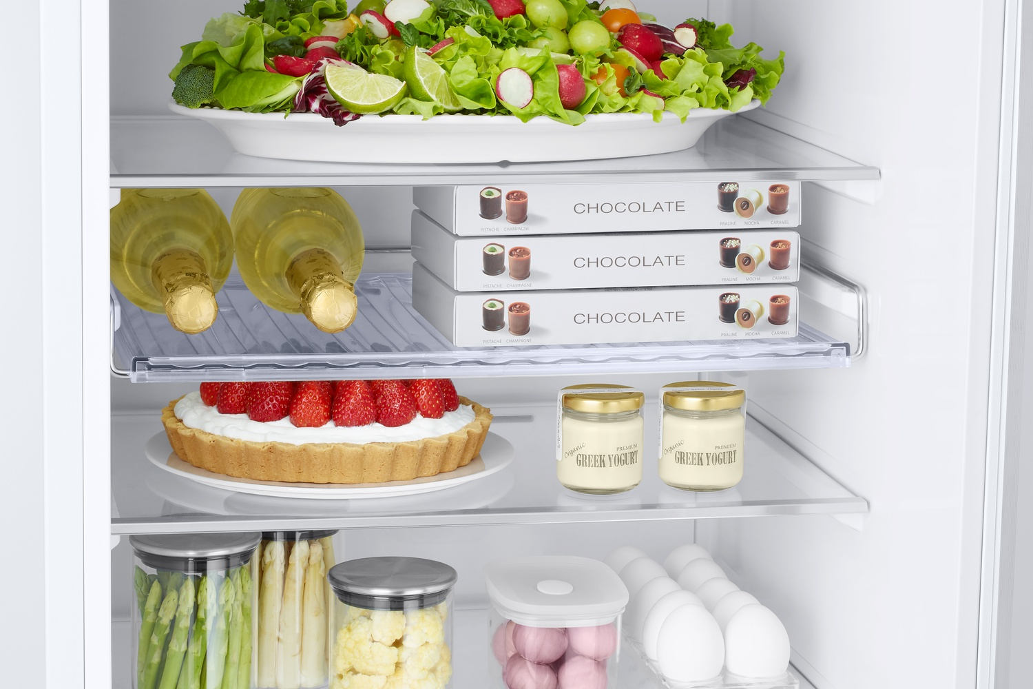 Estantes de refrigerador llenos: ensalada, chocolate, pastel, yogur, verduras y huevos.
