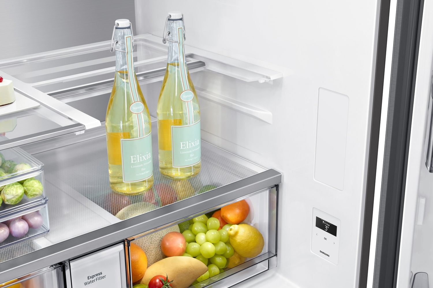 Dentro de un refrigerador: dos botellas de limonada Elixia, coles de Bruselas, uvas, naranjas, mango y limones.