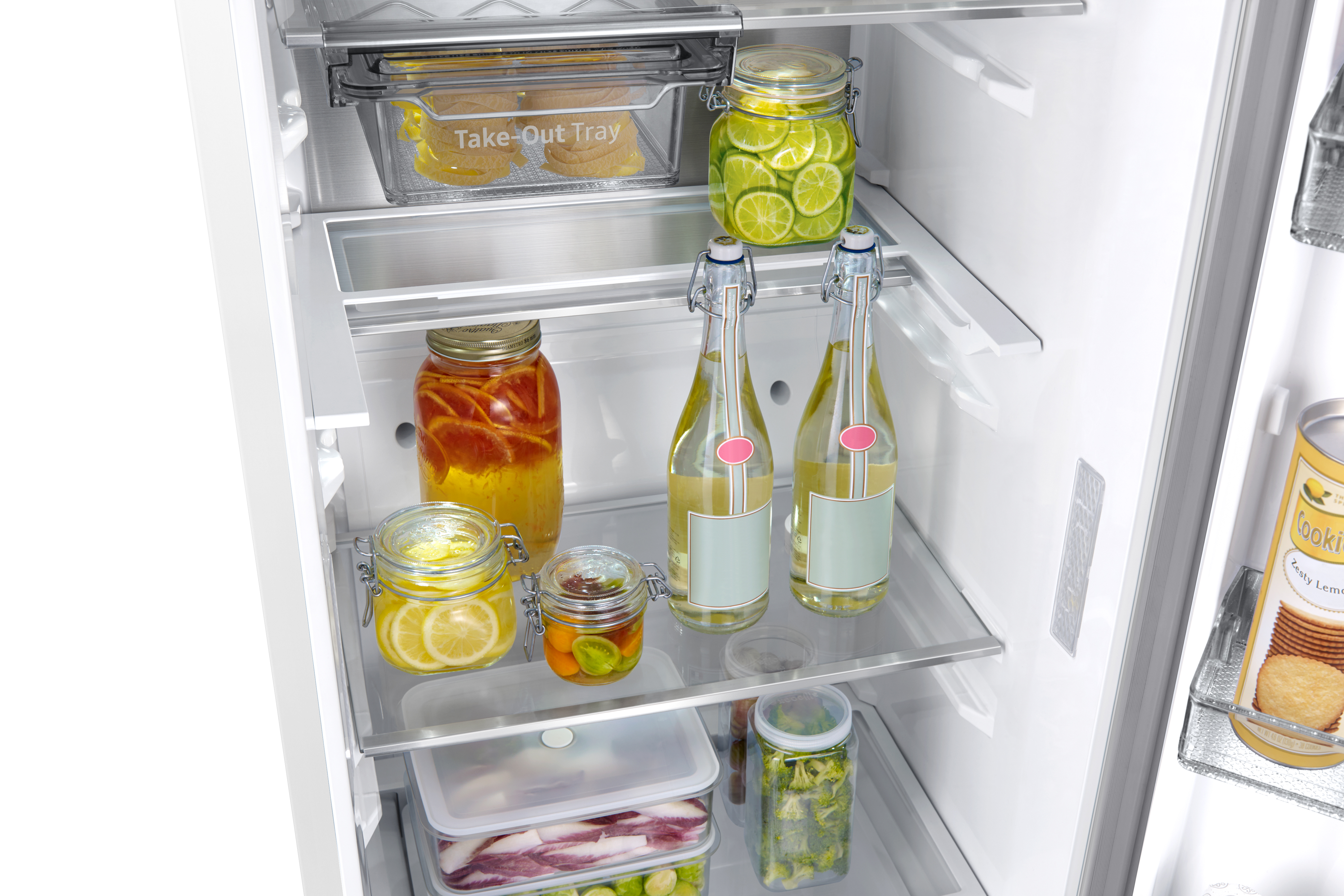 Dentro de un refrigerador: frascos de pepinillos, limones, limas, botellas de bebida y una lata de galletas.