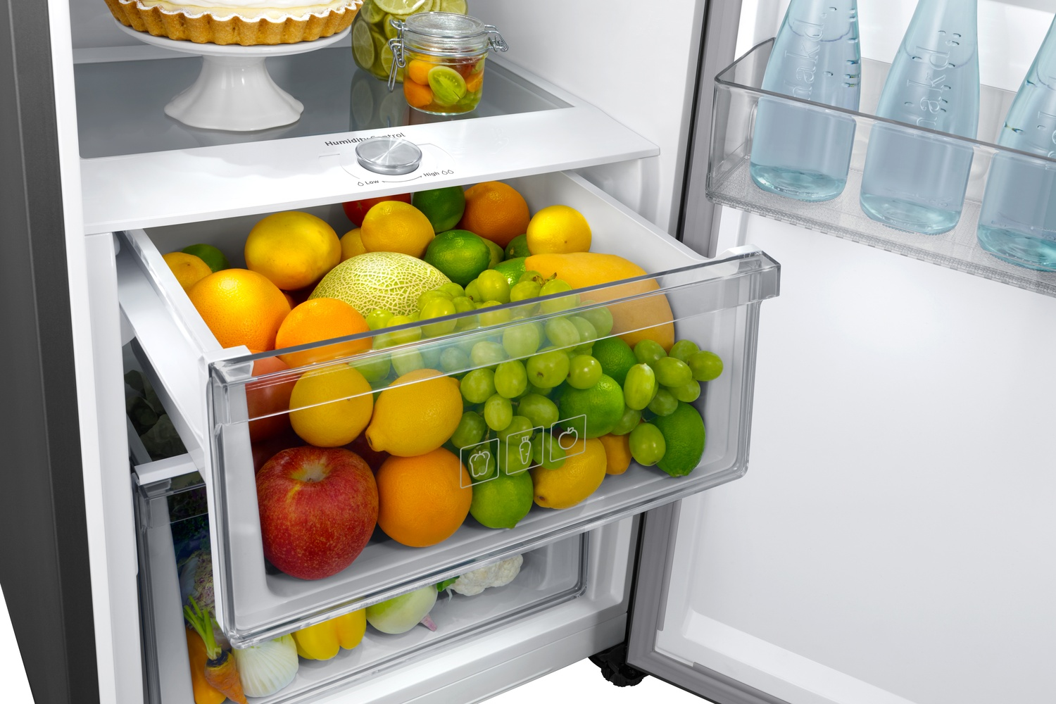 Un cajón de refrigerador lleno de fruta: manzanas, naranjas, limones, melón, uvas y limas.