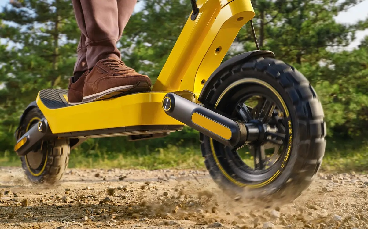 Osoba jedzie żółtym skuterem elektrycznym po piaszczystej ścieżce.
