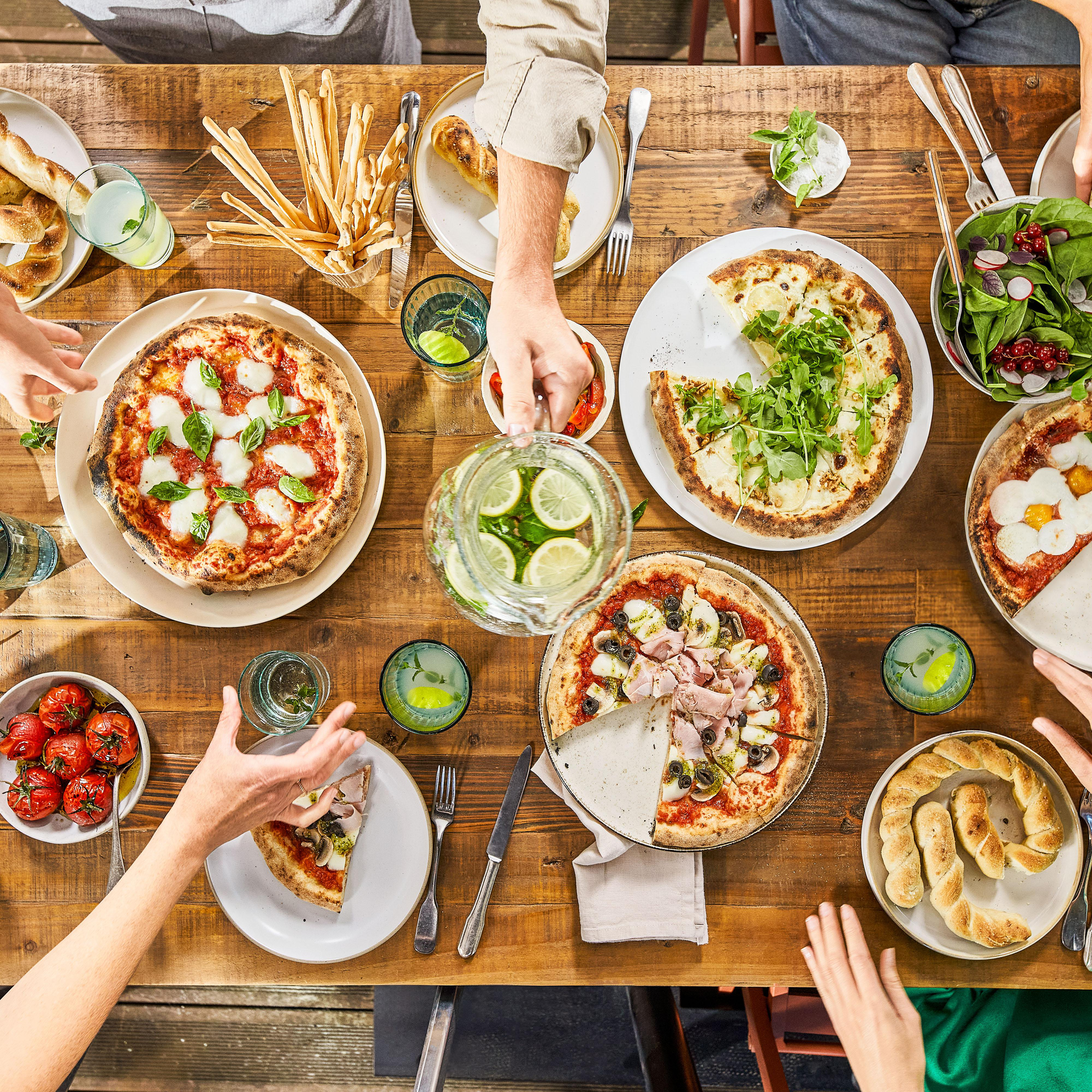 Eine Gruppe von Menschen isst Pizza und Salate an einem Holztisch.