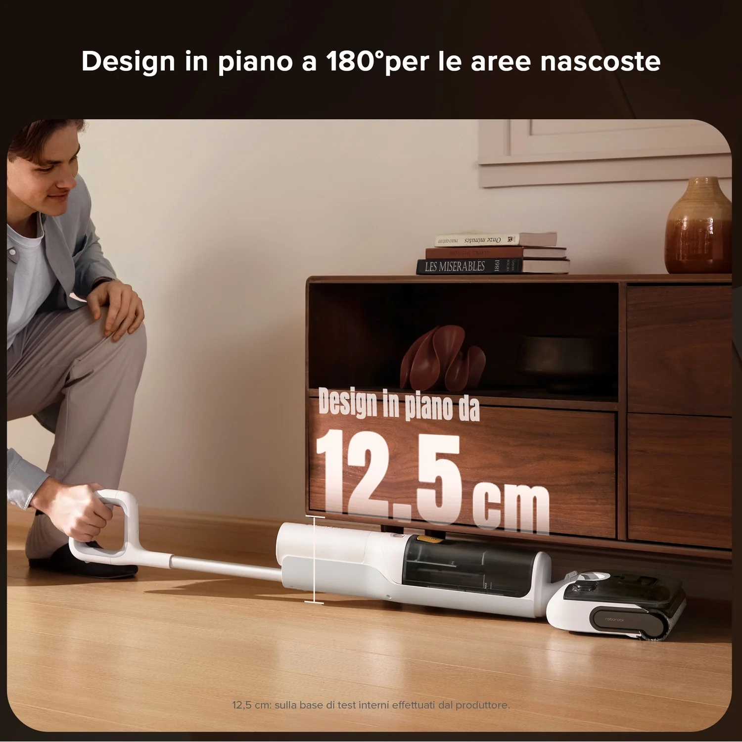 Uomo in ginocchio vicino a un pulitore per pavimenti bianco che passa sotto un mobile.