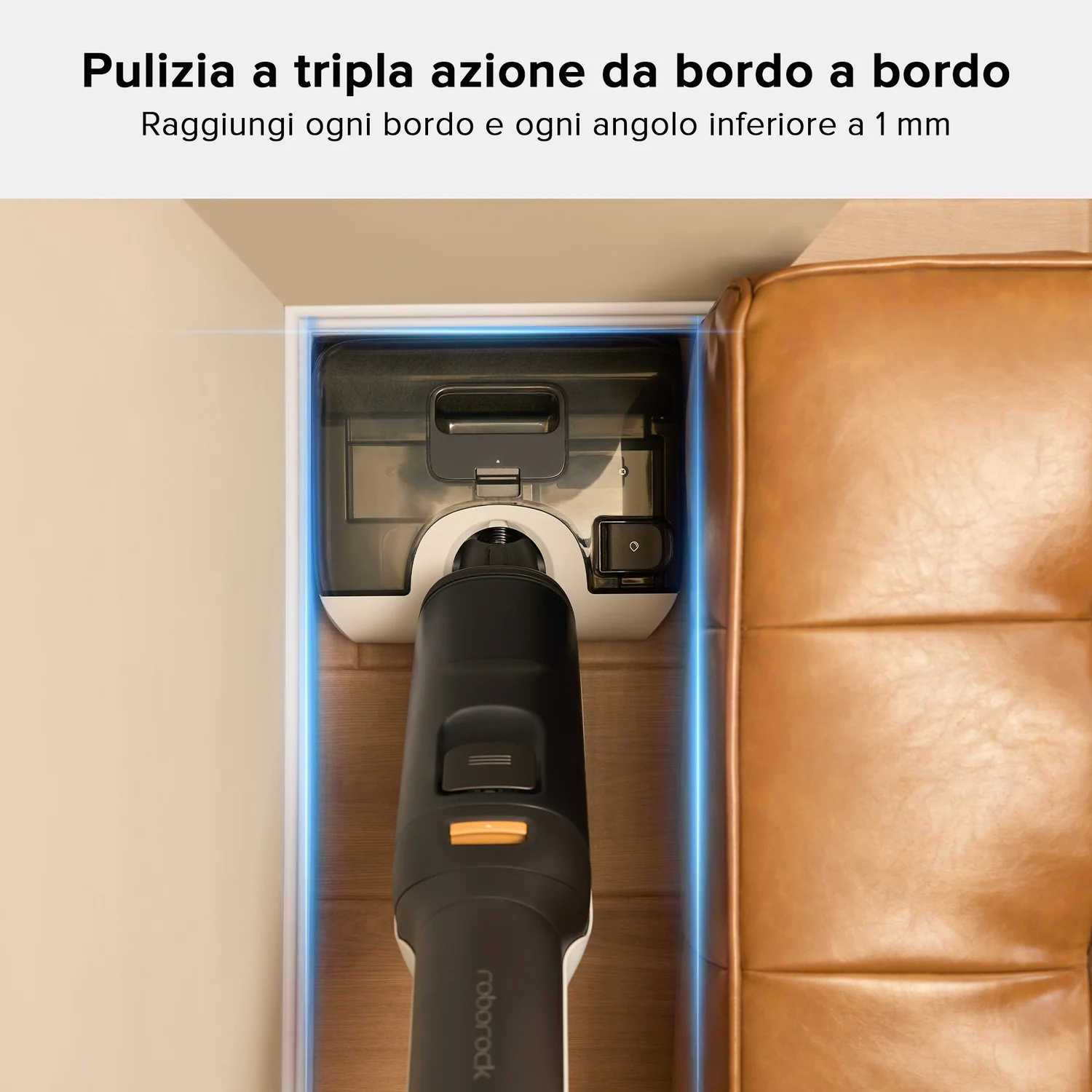 Un aspirapolvere pulisce lungo un muro e un divano in pelle marrone.