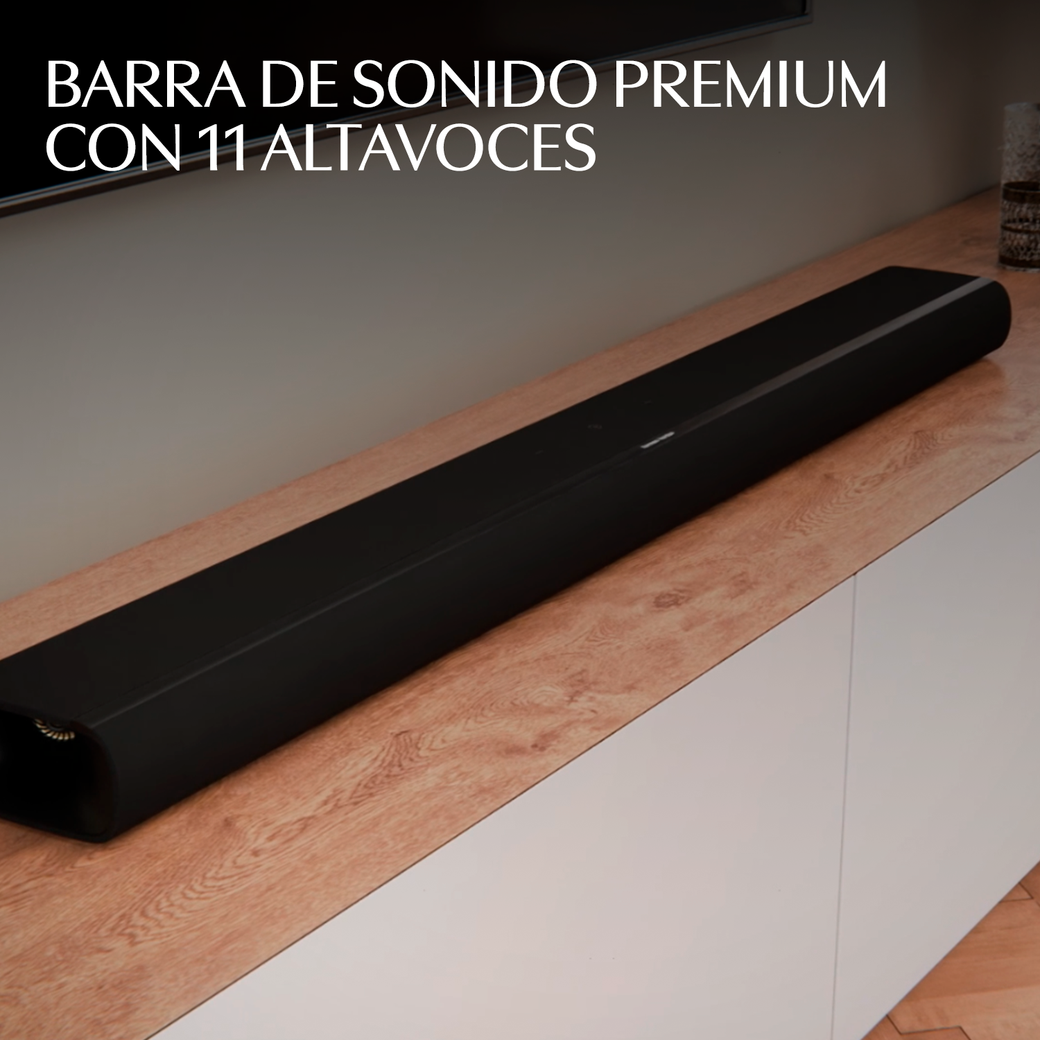 Una barra de sonido negra con 11 altavoces descansa sobre un mueble de madera.