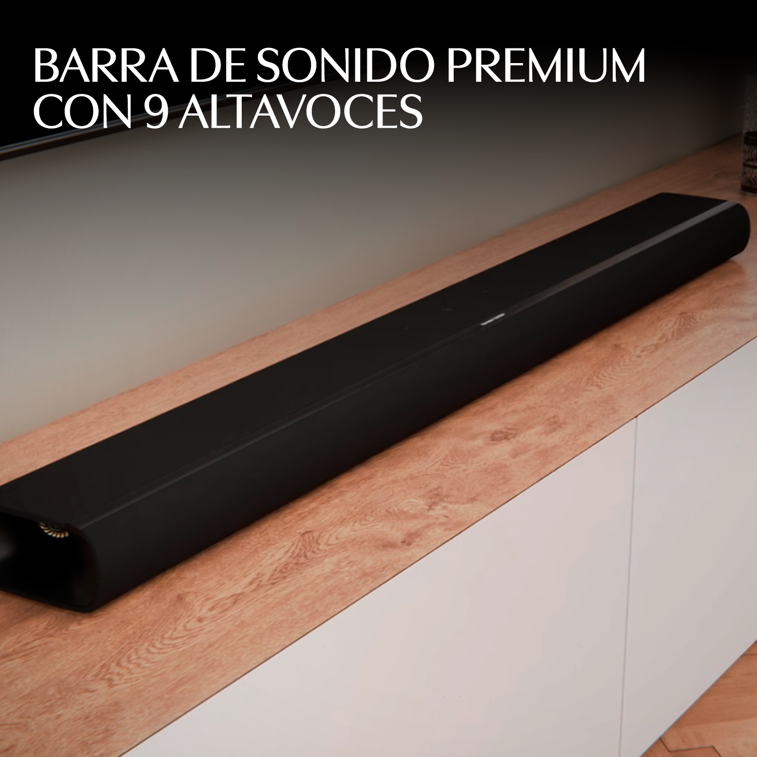 Barra de sonido negra y larga sobre superficie de madera con gabinetes blancos.