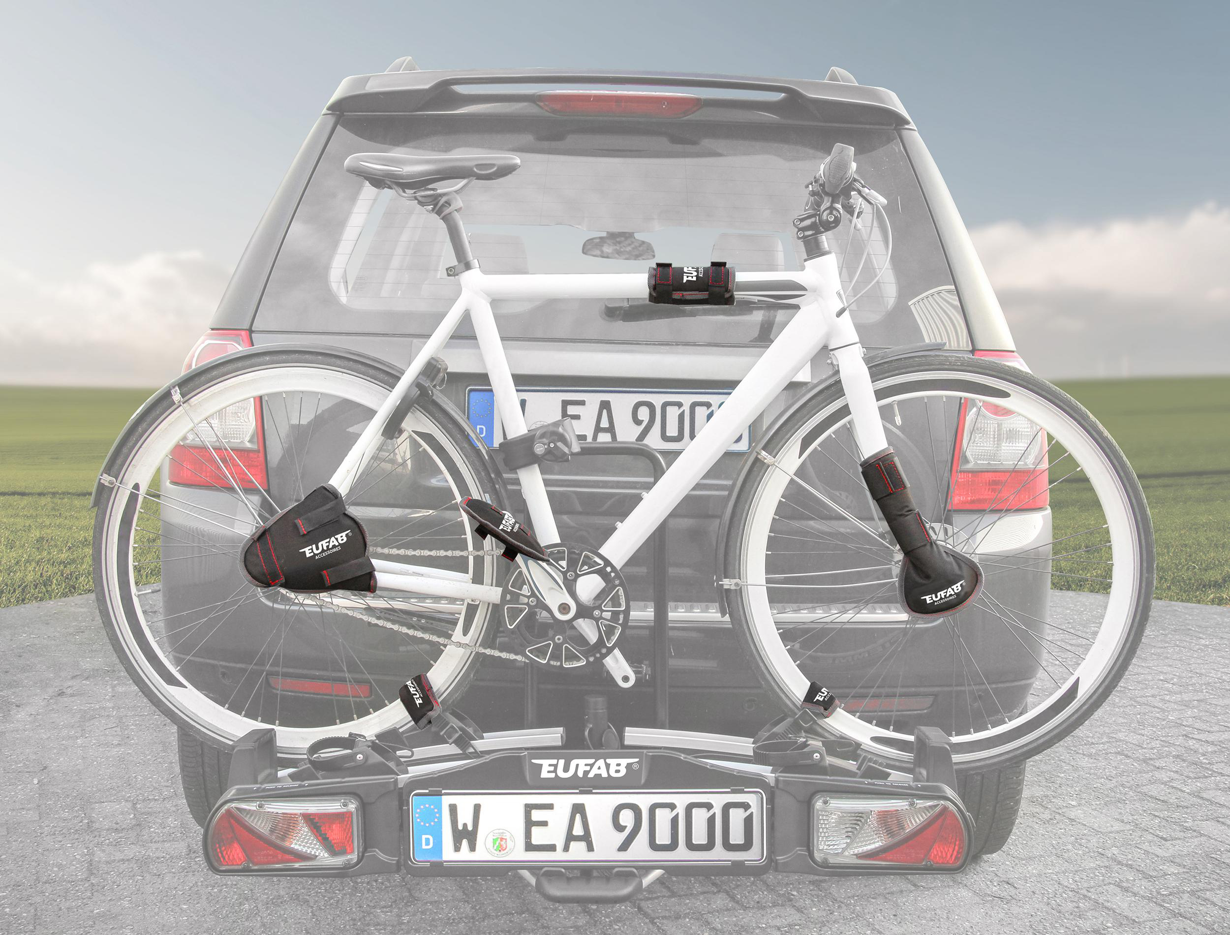 Ein weißes Fahrrad auf einem Heckträger am Auto, mit Landschaft im Hintergrund.