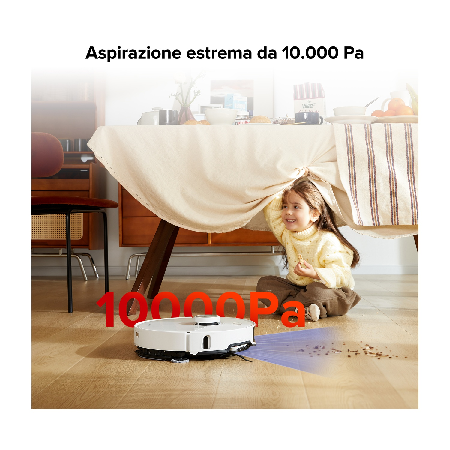 Un robot aspirapolvere bianco pulisce un pavimento in legno davanti a una bambina seduta sotto un tavolo.