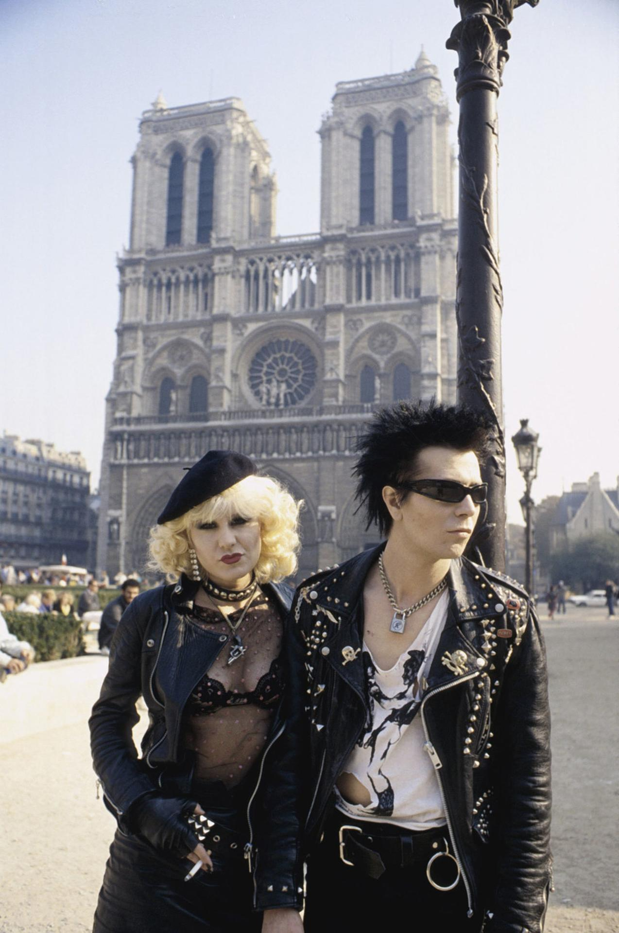 Ein Punkpaar steht vor Notre Dame in Paris. Sie tragen Lederjacken und auffällige Kleidung.