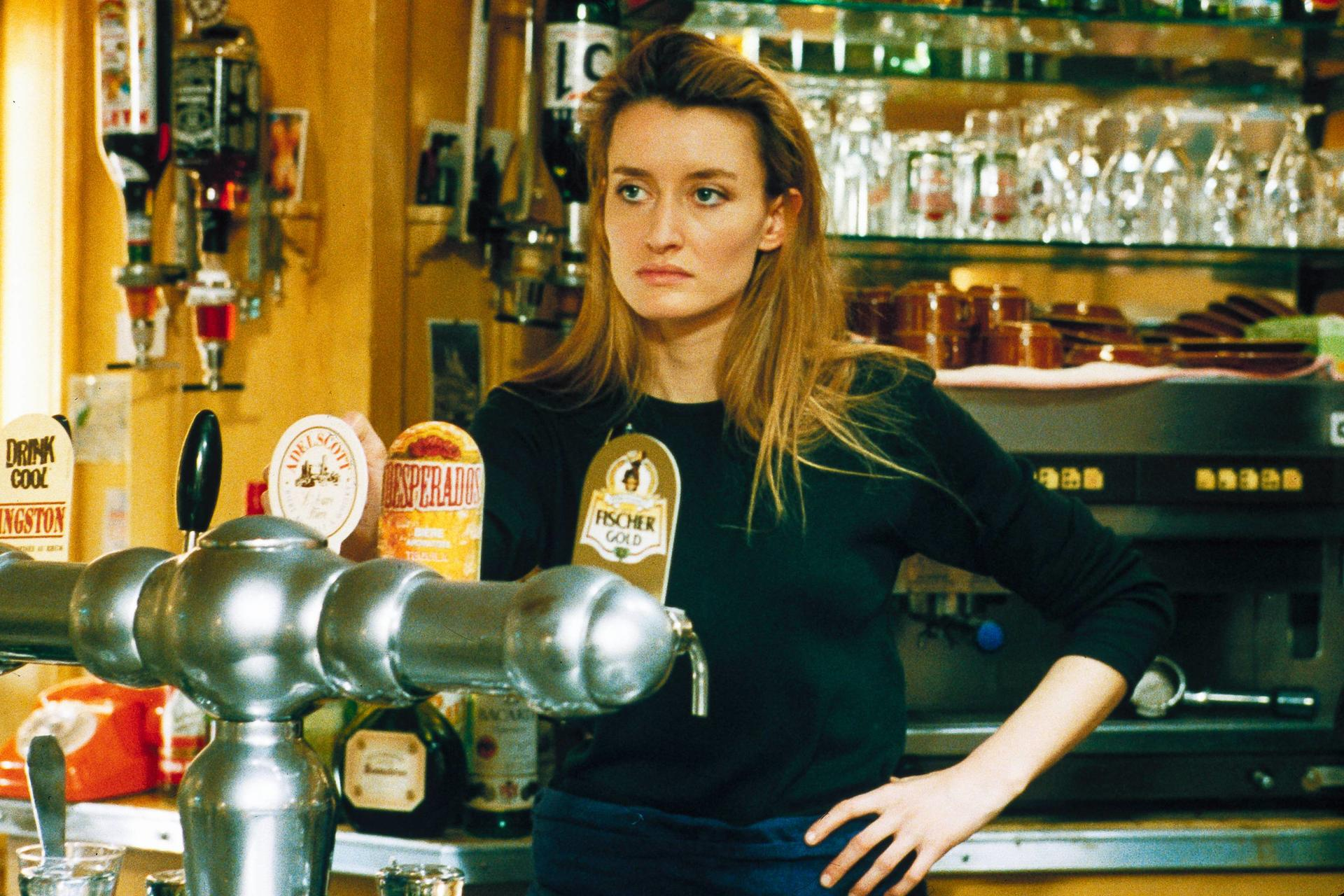 Eine Frau steht hinter einer Bar mit Zapfhähnen und Flaschen.