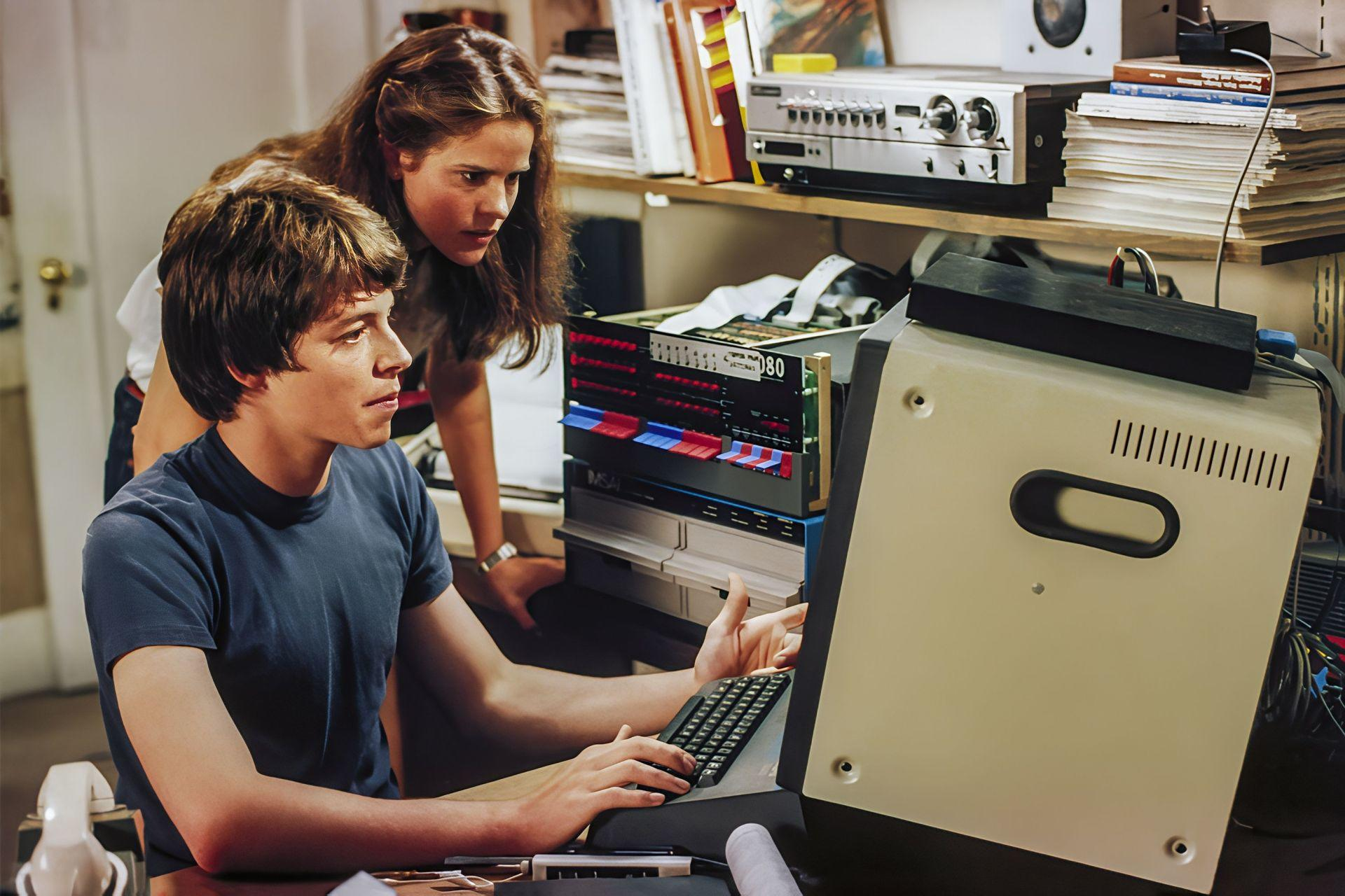 Ein Mann und eine Frau schauen auf einen Computer und eine Tastatur.