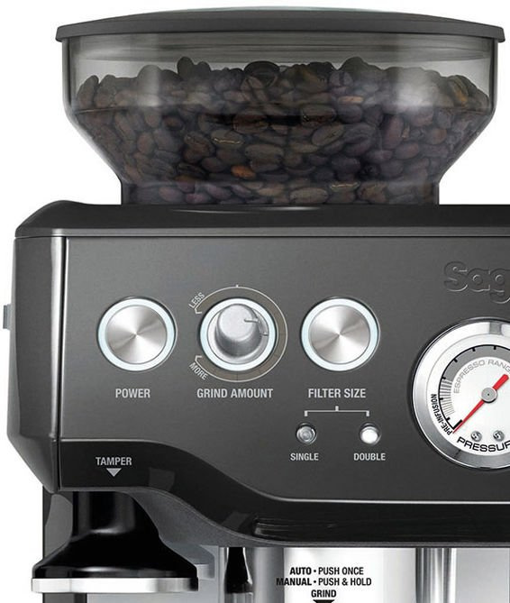 Zbliżenie szarej ekspresu Sage z ziarnami kawy w zasobniku i pokrętłami sterującymi.