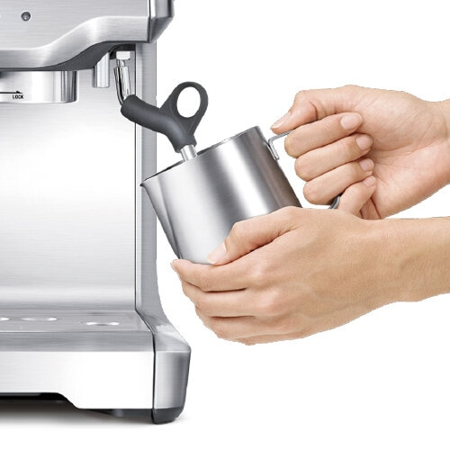 Osoba spieniająca mleko w metalowym dzbanku za pomocą ekspresu do kawy.