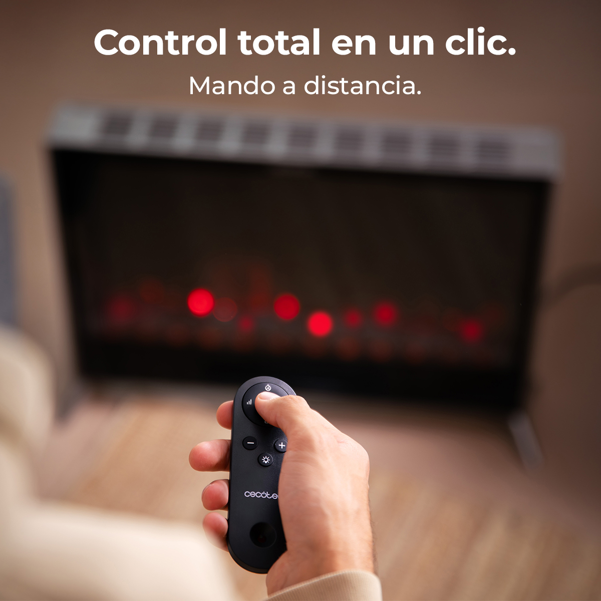 Una mano sostiene un mando a distancia delante de una chimenea borrosa con llamas rojas.