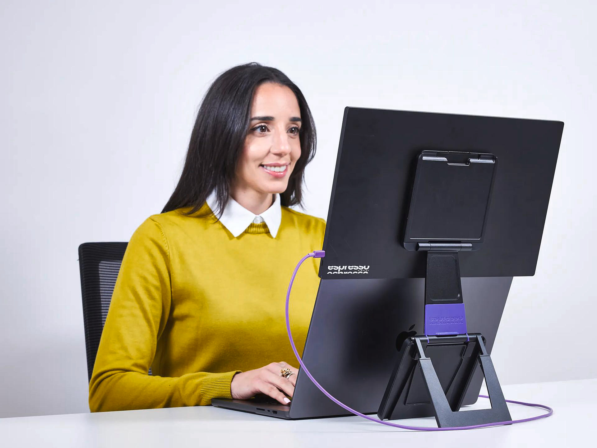 Eine Frau sitzt an einem Schreibtisch und blickt auf einen Laptop und einen externen Monitor.