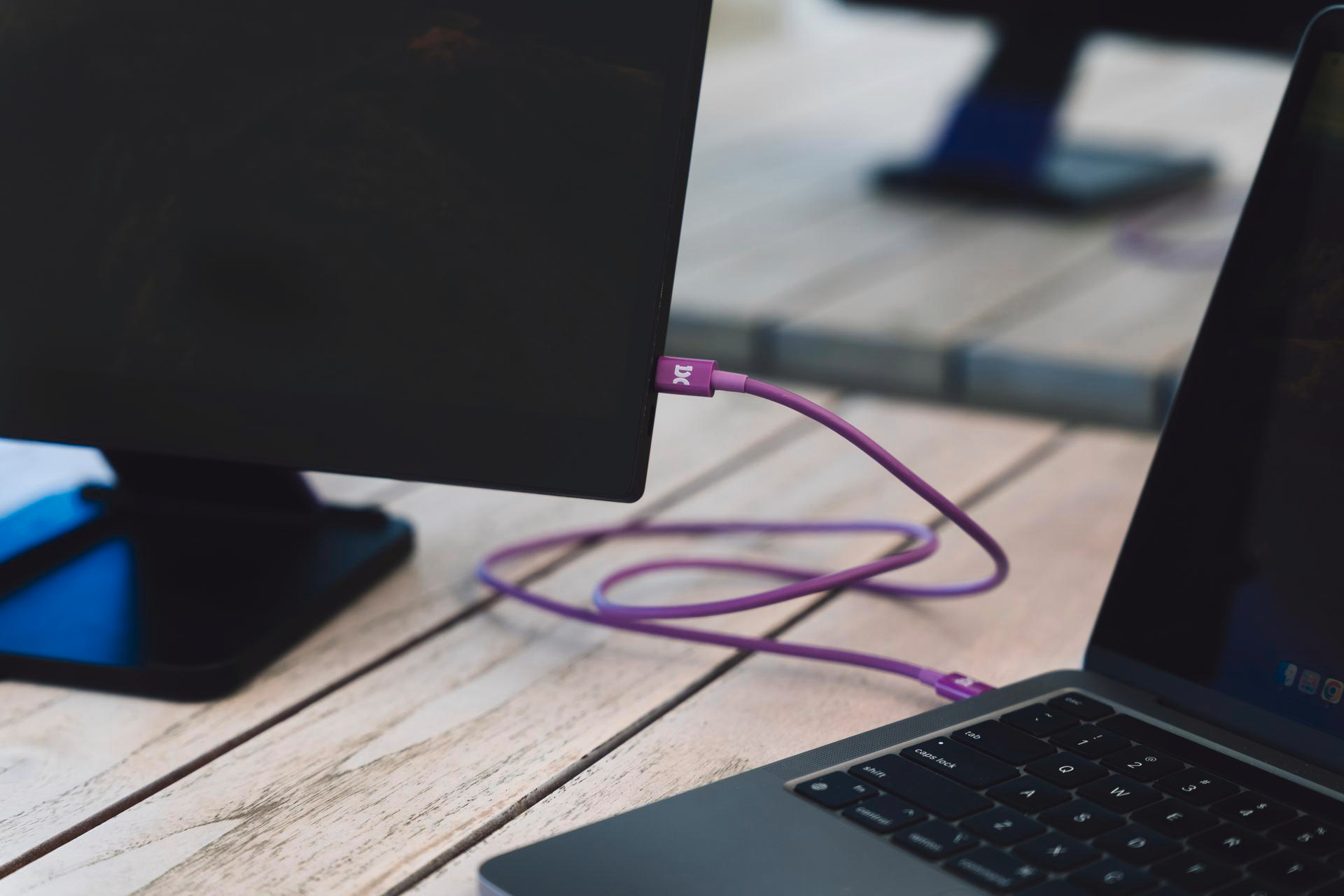 Ein violetter USB-C-Kabel verbindet einen Monitor mit einem Laptop.