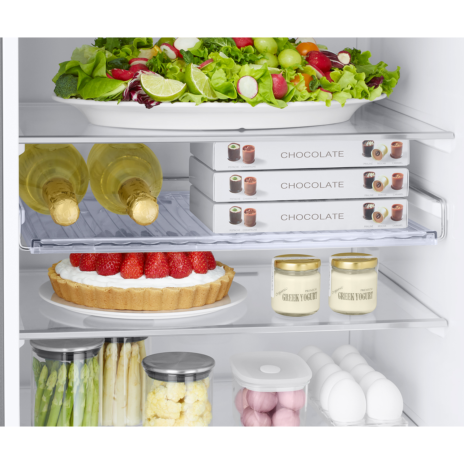 Una repisa de refrigerador con ensalada, champán, chocolates, tarta, yogur, huevos y verduras.