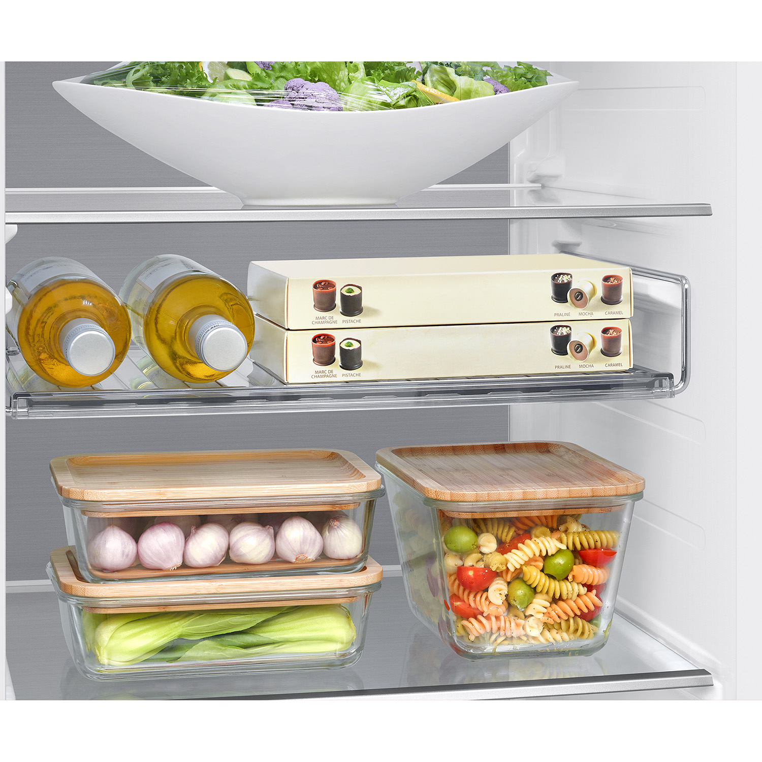 Interior de refrigerador con comida: ensalada, botellas, chocolates, ajo, verduras y ensalada de pasta.