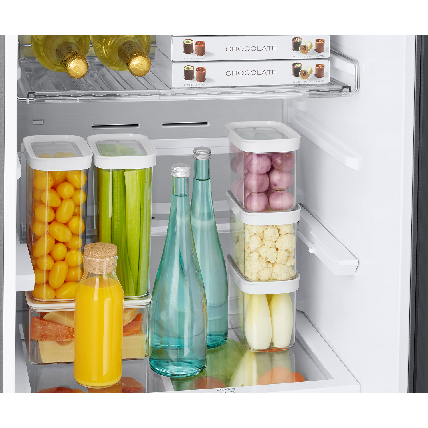 Interior de refrigerador con botellas, recipientes con verduras, jugo y queso.