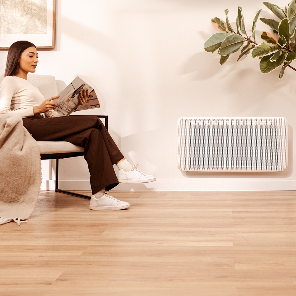 Una mujer lee en un sillón junto a un radiador montado en la pared.