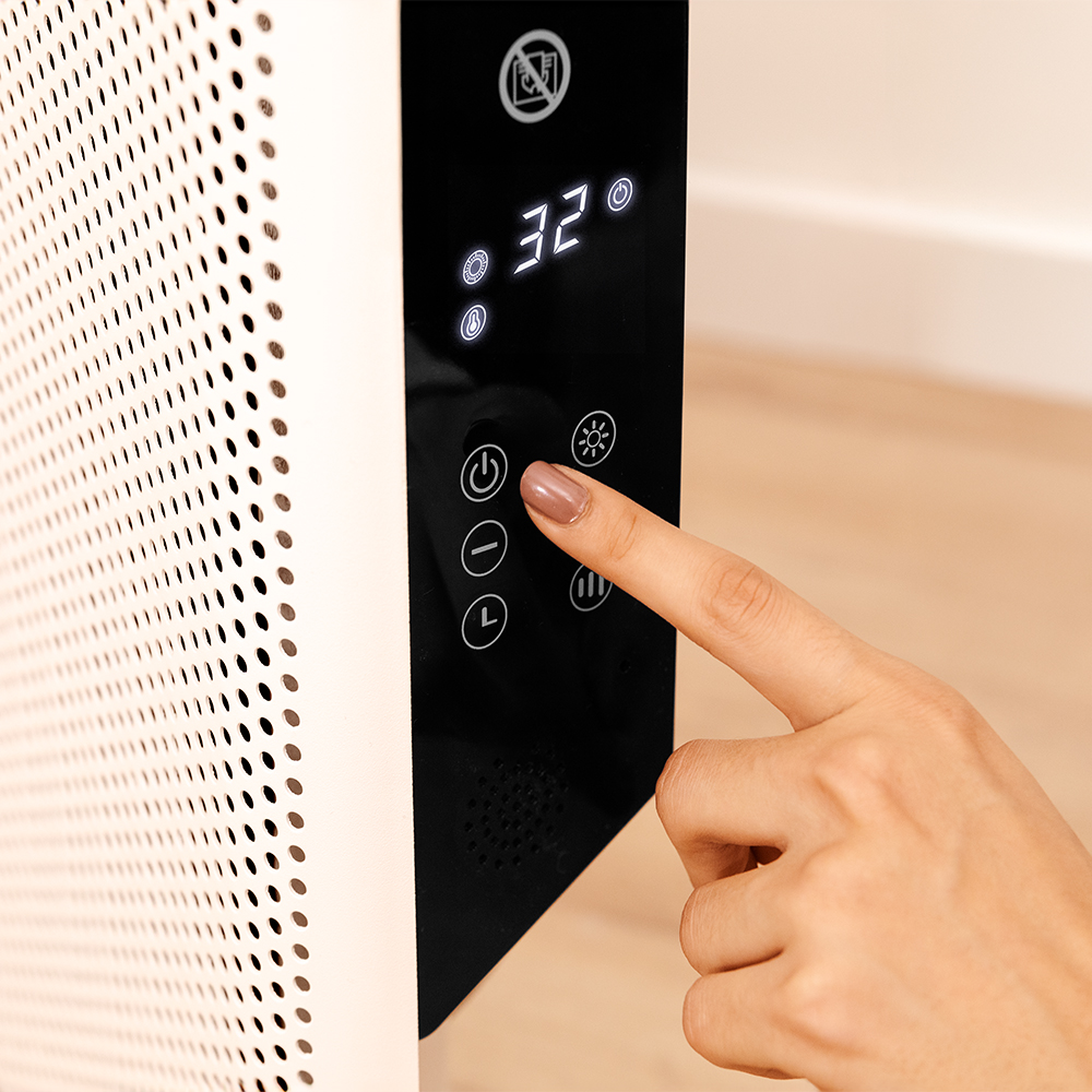 Una mano presiona el botón de encendido de un calefactor con pantalla digital.