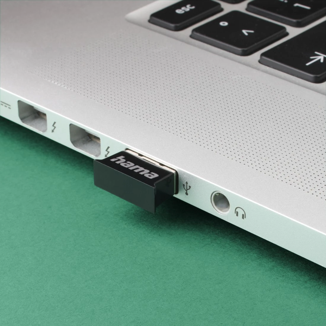 Ein schwarzer Hama USB-Adapter steckt in einem silbernen Laptop.