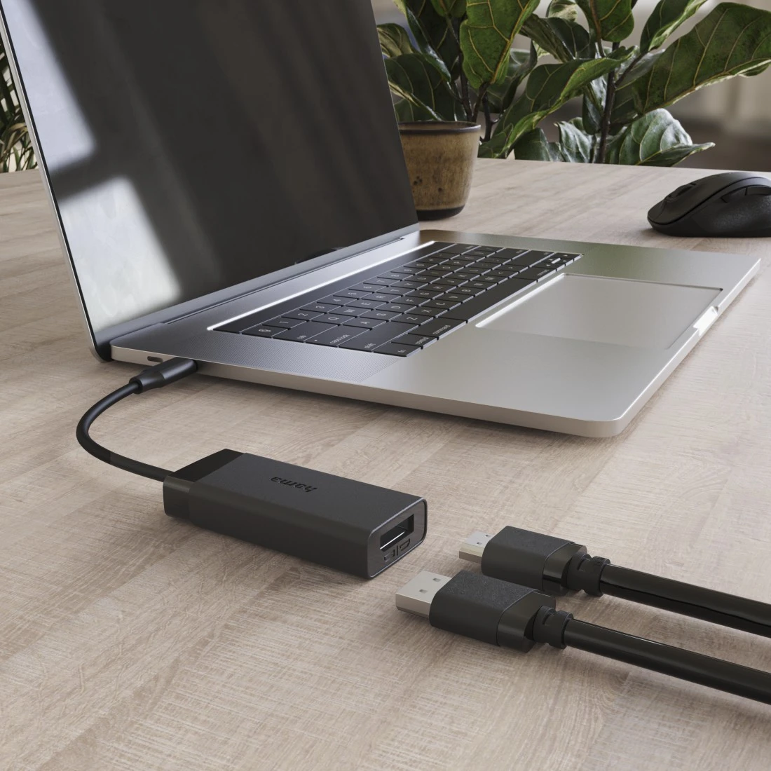 Ein schwarzer USB-Hub wird an einen Laptop angeschlossen, zwei schwarze USB-Kabel liegen daneben auf einem Holztisch.
