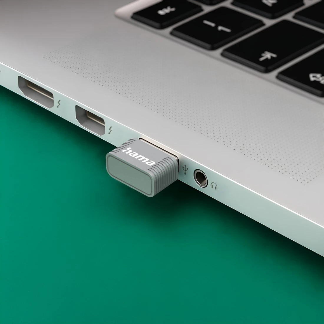 Una chiavetta USB grigia è inserita in un laptop, accanto a un jack per cuffie.