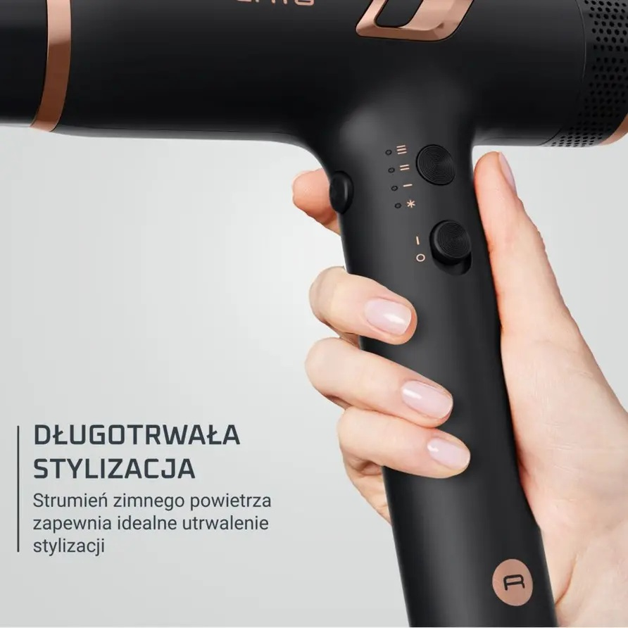Dłoń trzyma czarną suszarkę do włosów z miedzianymi akcentami i przyciskami sterującymi.