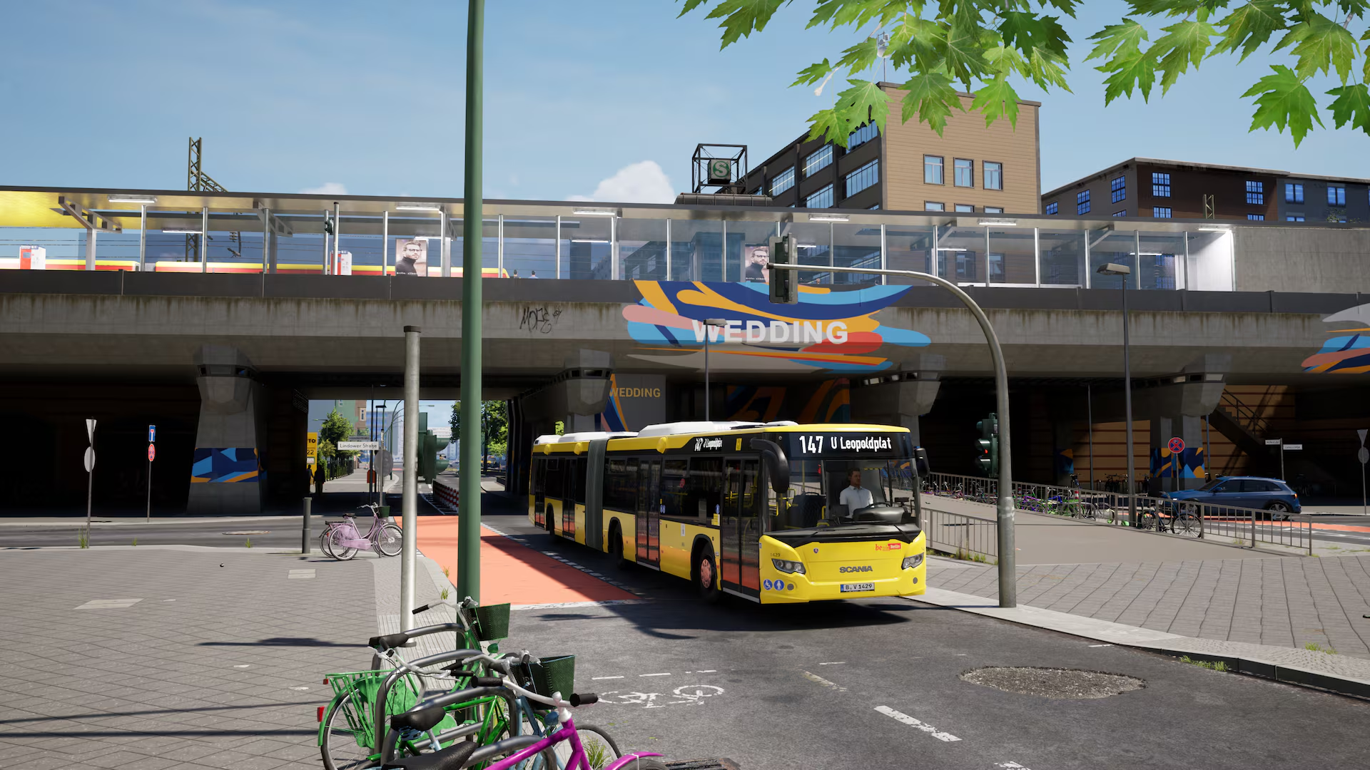 Un bus articulé jaune passe sous une ligne de train aérienne. Bâtiments gris en arrière-plan.
