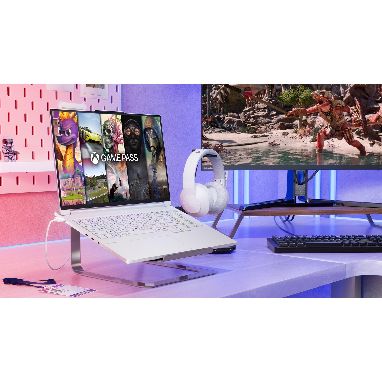 Un laptop bianco mostra GAME PASS accanto a un monitor con scena di gioco.