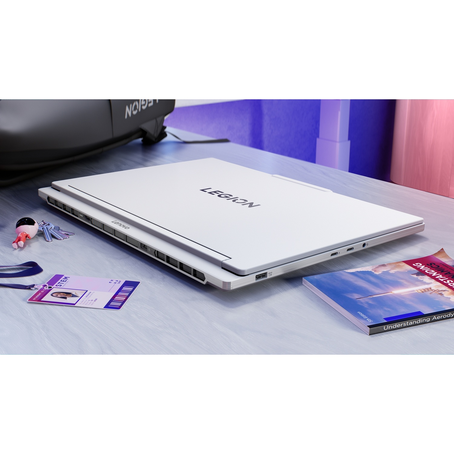 Un laptop bianco con logo "Legion" su scrivania vicino a chiavi, tesserino e libro.