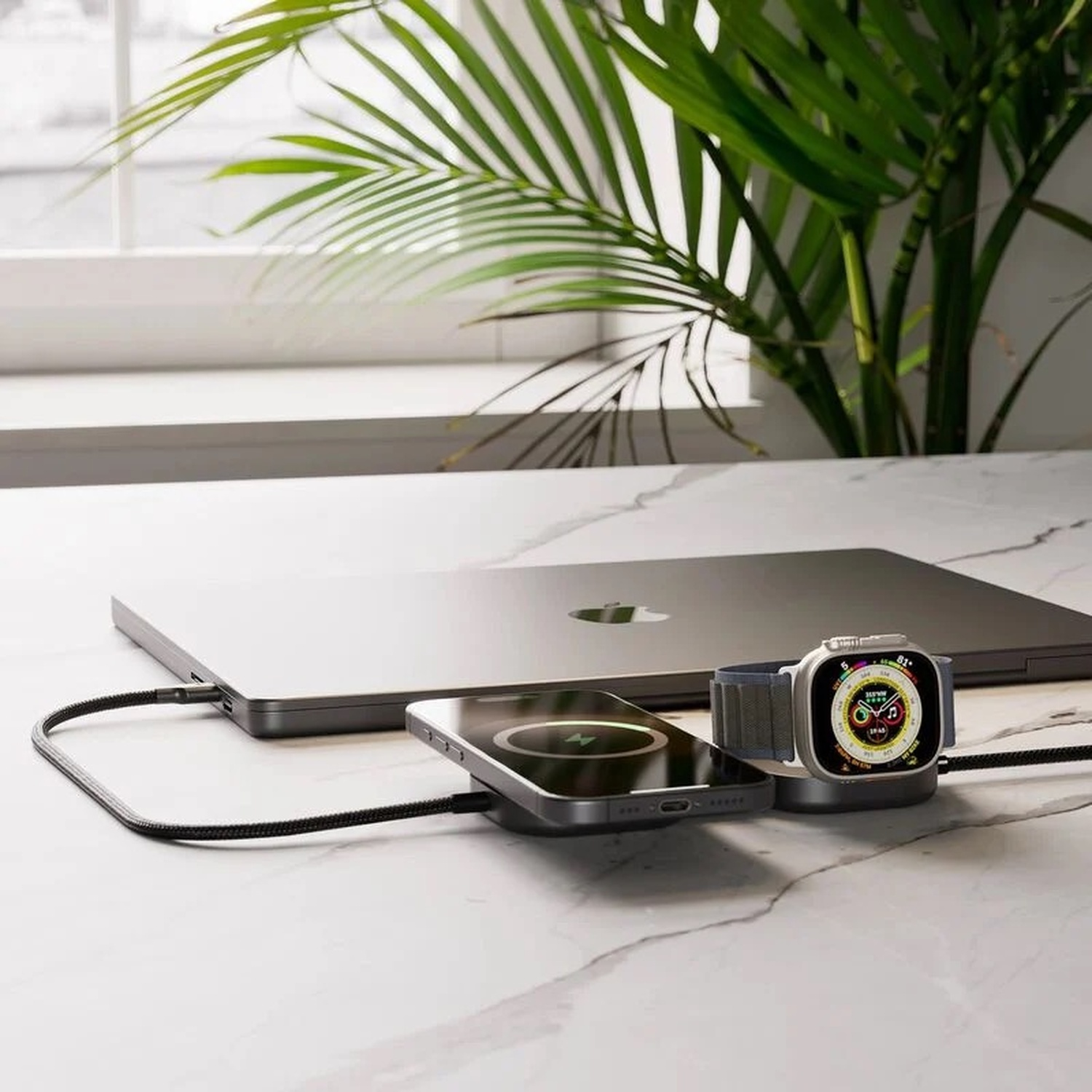 Un laptop, un telefono e un orologio si caricano su una superficie di marmo.