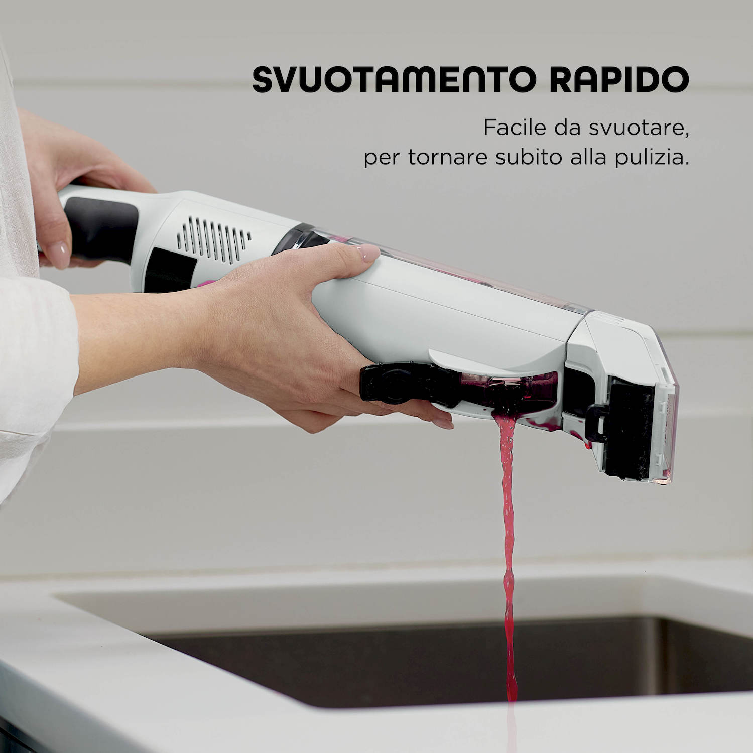 Una mano svuota un apparecchio bianco con liquido rosso in un lavandino.