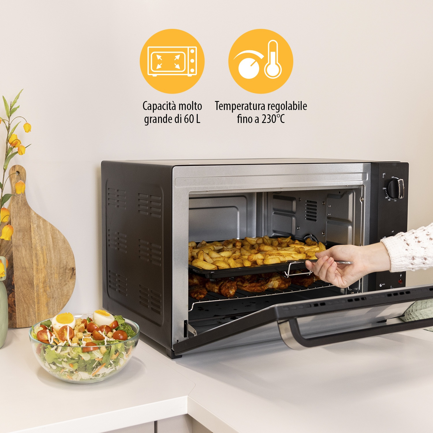 Una persona toglie una teglia di patatine e pollo da un forno. Accanto c'è un'insalata.