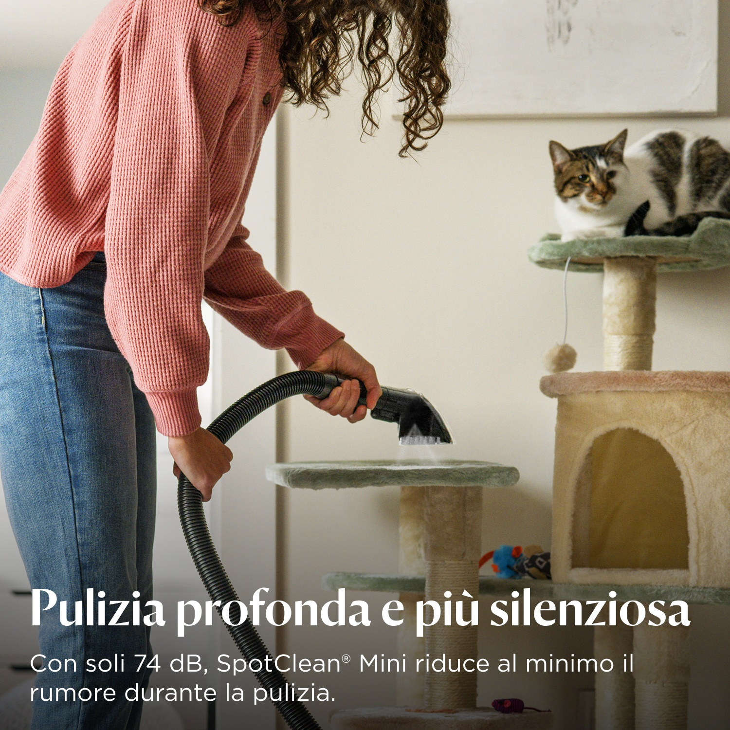 Una persona aspira vicino a un tiragraffi dove è seduto un gatto.