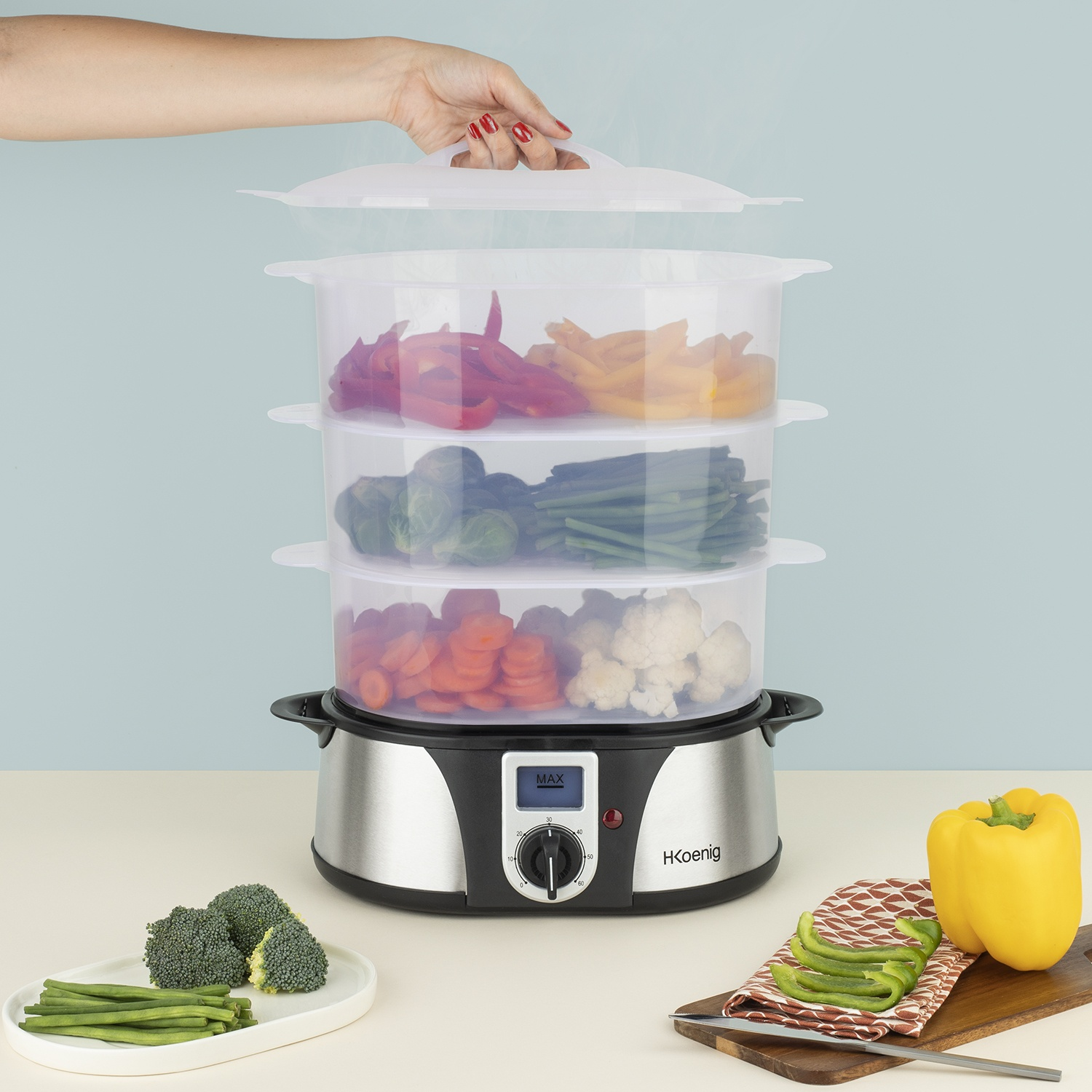 Un vaporiera a tre livelli con verdure. Una mano apre il coperchio.