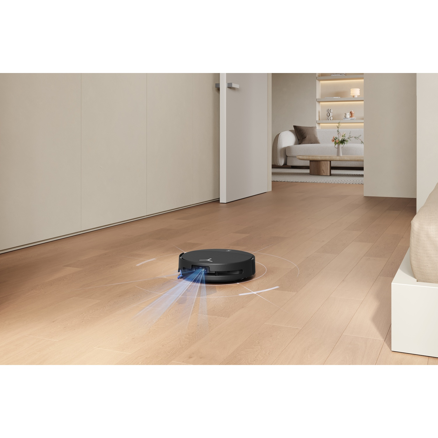 Un robot aspirapolvere nero pulisce un pavimento in legno in un soggiorno moderno.