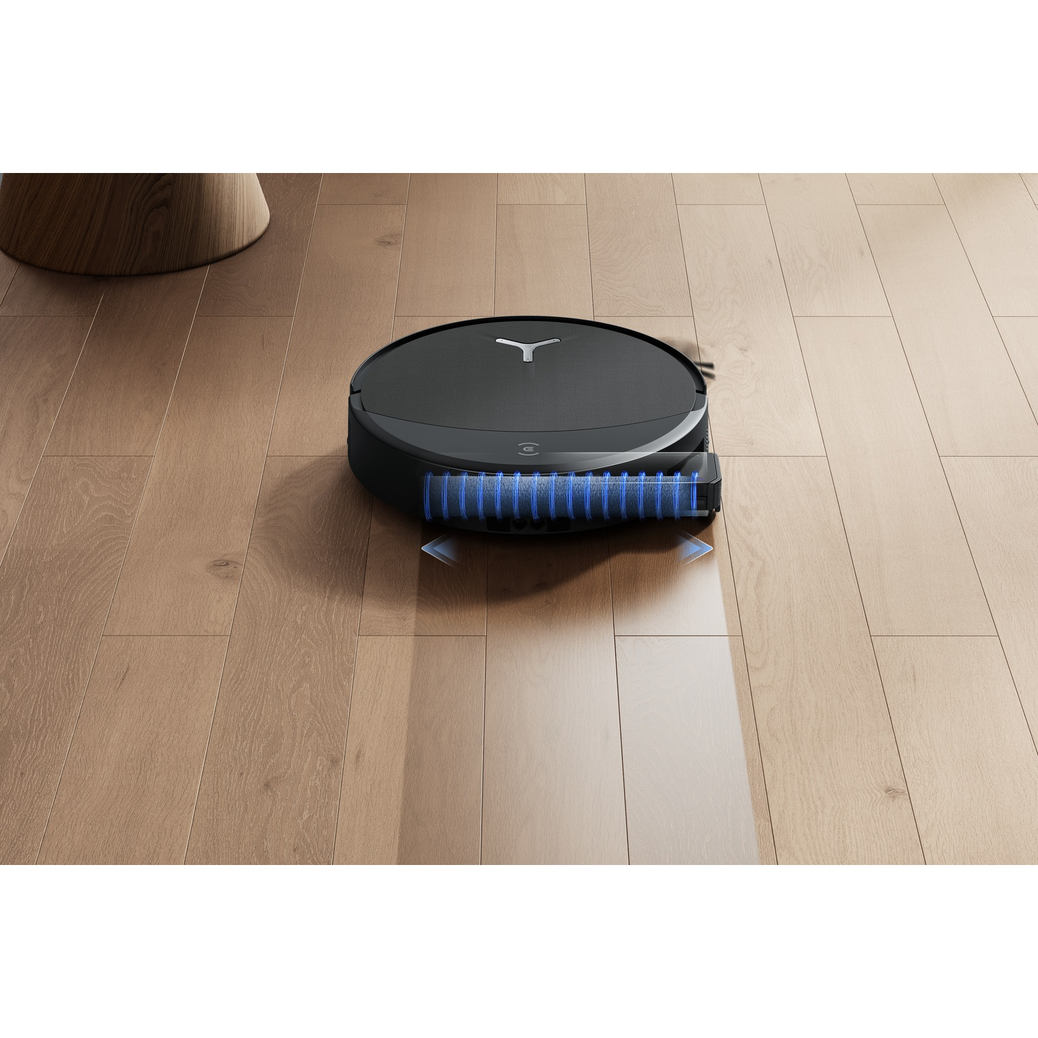 Un robot aspirapolvere nero pulisce un pavimento in legno con spazzole blu.